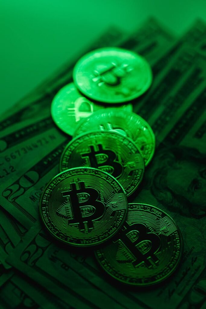 A stack of Bitcoin coins atop US dollar bills illuminated by green lighting, symbolizing digital finance and cryptocurrency.